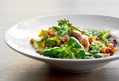 Plato de ensalada de pollo con hojas de moringa y queso parmesano.