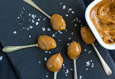 Varias cucharadas de dulce de leche cremoso con cristales de sal marina, un alimento de origen mineral, esparcidos sobre una superficie oscura