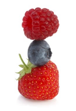Una frambuesa en equilibrio sobre un arándano con una fresa en la base, sobre un fondo blanco.