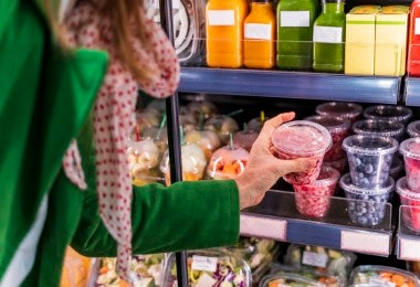 Mujer sacando bayas envasadas del estante de refrigeración en una tienda.