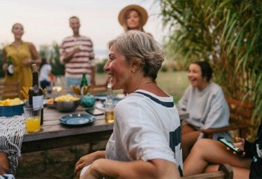 Fotografía de una mujer disfrutando de una cena al aire libre con sus comensales.