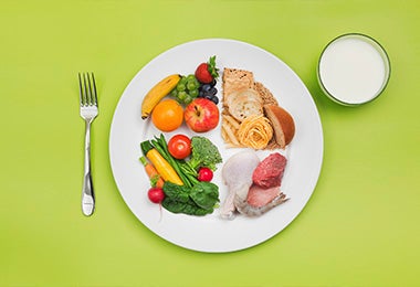 Un plato con verduras, frutas, carnes, pastas y otras comidas para una dieta balanceada con proteínas magras.