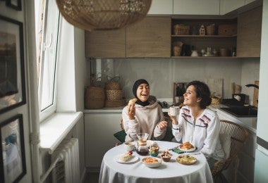 Dos chicas multirraciales felices desayunando y tomando café juntas en casa. Una amistad multicultural. Una lleva hiyab.