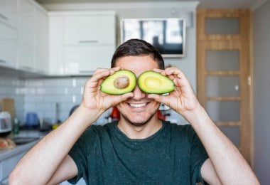 Joven divirtiéndose con aguacate en la cocina.