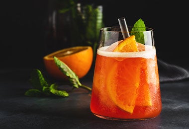 Vaso de jugo de borojó con pedazo de borojó partido a la mitad al fondo.