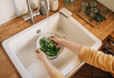 Manos femeninas lavando espinacas en el fregadero de la cocina por inocuidad.