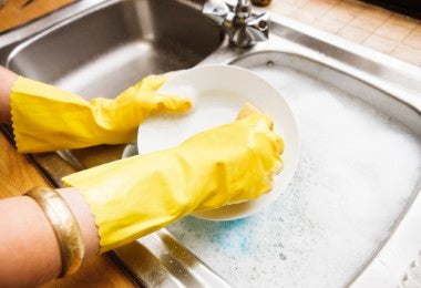 Una mujer con guantes de goma lava los platos.