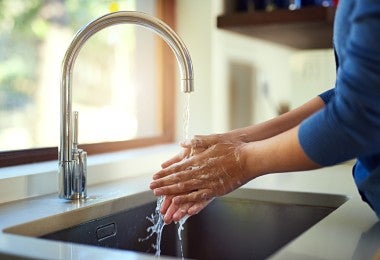 Imagen de una mujer lavándose las manos en el fregadero de la cocina.