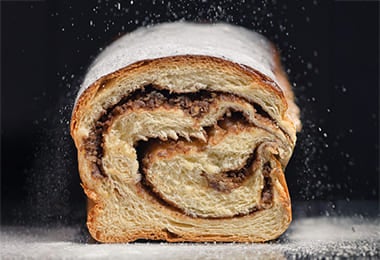 Pan relleno de chocolate siendo espolvoreado con azúcar glas.