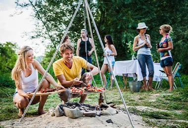 Grupo de personas cocinando al aire libre en parrilla colgante de leña.