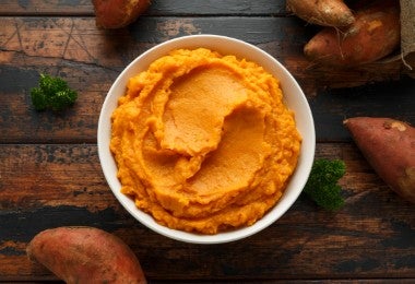 Puré de batatas en un tazón blanco sobre una mesa rústica de madera. comida sana.