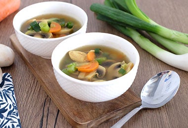 Dos tazones con sopa con hojas de diente de león, champiñones y zanahoria.