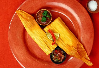 Tamales sazonados con achiote sobre plato rojo.