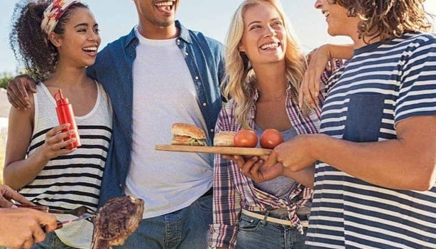 Grupo de amigos cocinando al aire libre carne y hamburguesas a la parrilla.