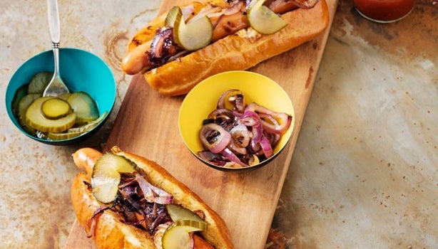 Vista de ángulo alto de una selección de 3 hot-dogs artesanales en panecillos de brioche con pepinillos.
