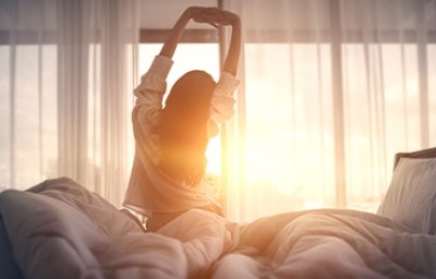 Una mujer con buenos hábitos de sueño estirando en la cama