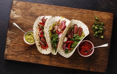 Tacos con jalapeños y ají casero sobre una tabla y un fondo negro