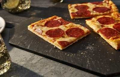 Porción de pizza de pepperoni con una masa delgada sobre un plato negro para celebrar su Día Mundial