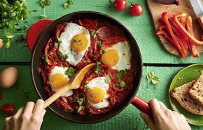 Huevos shakshuka con hierbas, salsa de tomate, pan y pimentón picado en toma cenital