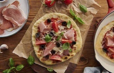 Mesa con pizza de prosciutto con aceitunas, tomates y rúgula