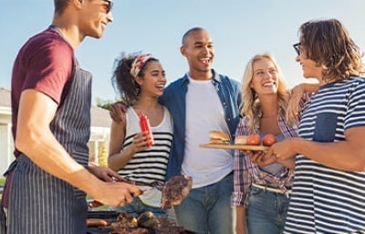Grupo de amigos cocinando al aire libre carne y hamburguesas a la parrilla.