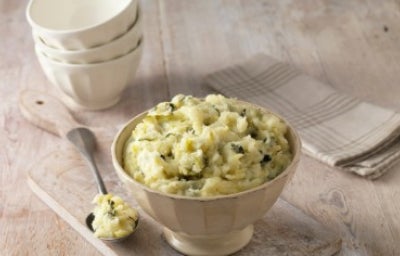 Puré de papa en un recipiente facetado color crema con cuchara de metal.