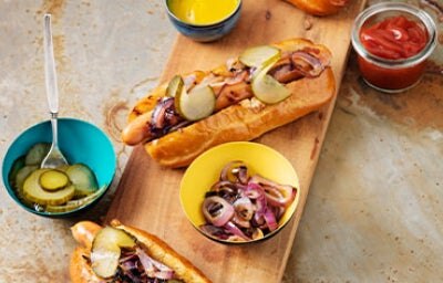 Vista de ángulo alto de una selección de 3 hot-dogs artesanales en panecillos de brioche con pepinillos.