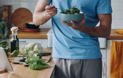 Hombre come ensalada de hojas de mostaza.