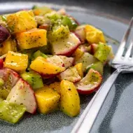 Una ensalada con mango y verduras, con su aderezo.