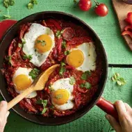 Huevos shakshuka con hierbas, salsa de tomate, pan y pimentón picado en toma cenital