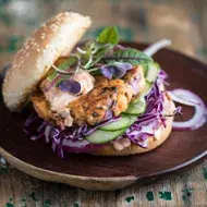 Apetitosa hamburguesa de pescado con vegetales emplatada y sobre una mesa de madera