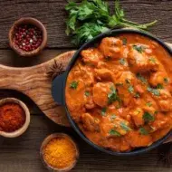 Butter Chicken con cilantro y acompañado de especias sobre tabla de madera