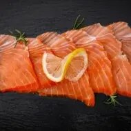 Pequeños trozos de salmón ahumado frío sobre fondo negro.