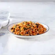 Plato hondo de arroz con habichuela junto a un tenedor, vaso de agua y servilleta.