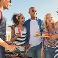 Cocinar al aire libre, la oportunidad de comer y compartir. Grupo de amigos cocinando al aire libre carne y hamburguesas a la parrilla.
