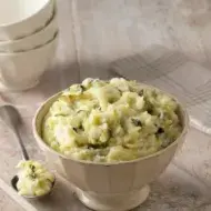Puré de papa en un recipiente facetado color crema con cuchara de metal.