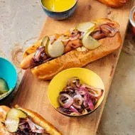 Vista de ángulo alto de una selección de 3 hot-dogs artesanales en panecillos de brioche con pepinillos.