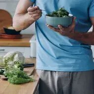 Hombre come ensalada de hojas de mostaza.