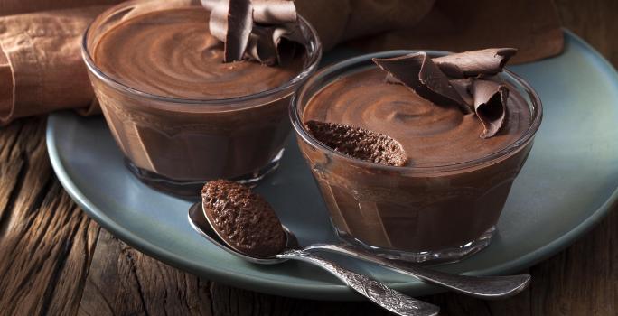 Foto de dos tazones pequeños con mousse de chocolate adentro encima de un plato azul